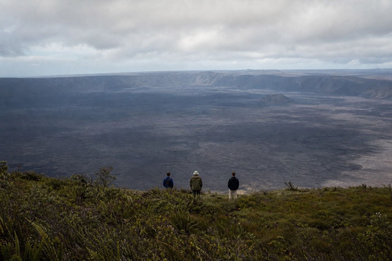 Hikers on the rim trail above the vast black caldera of Sierra Negra volcano on Isabela Island, cloud drifting across the far wall