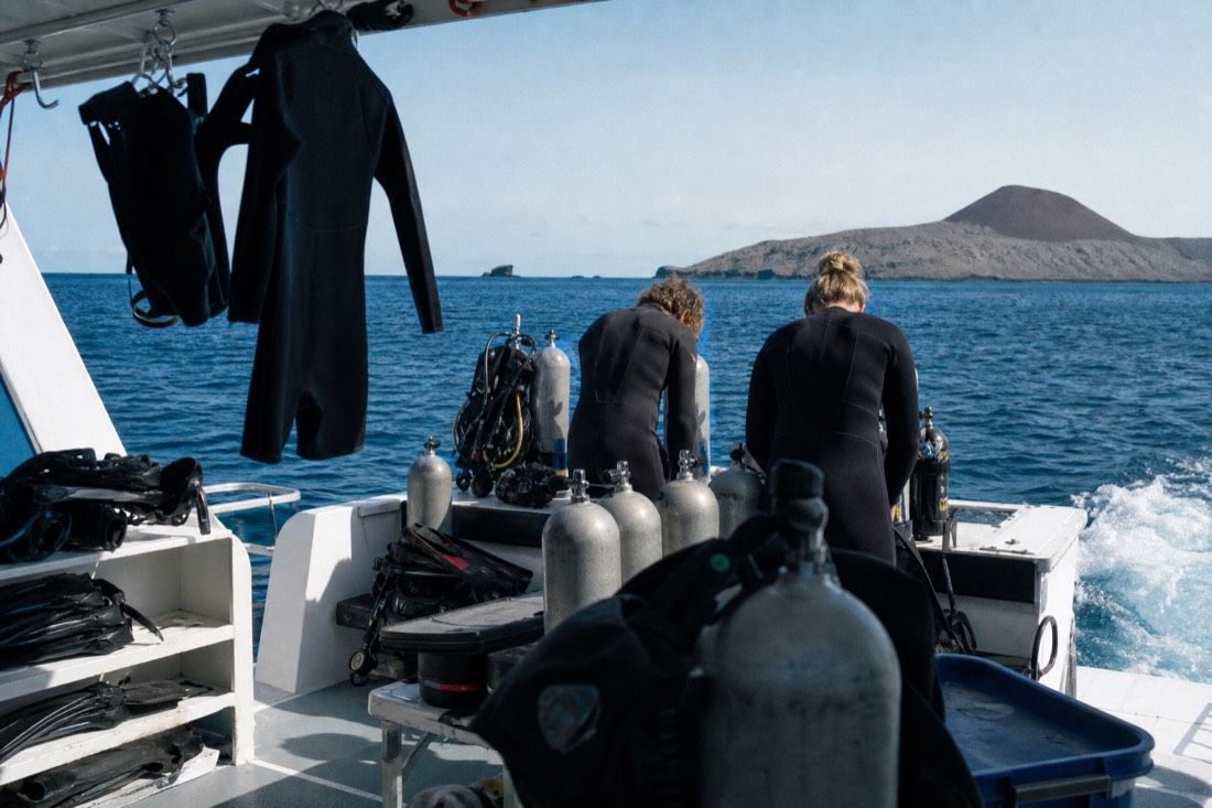 Divers in wetsuits preparing tanks on the back deck of a small Galapagos dive boat