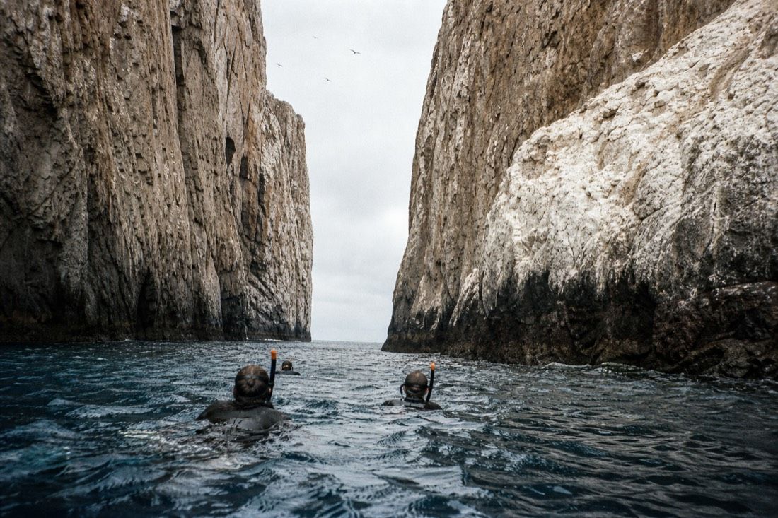 Snorkellers drifting through the narrow channel between the two halves of Kicker Rock